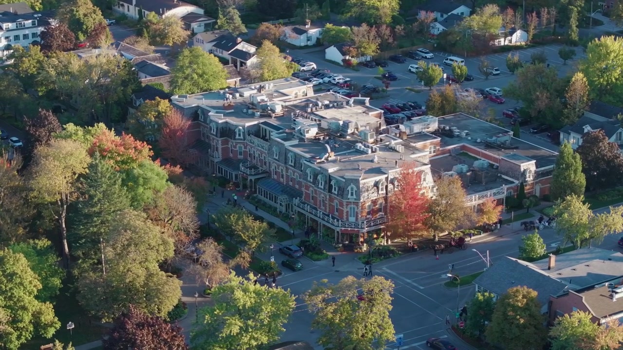 A close-up drone orbit around the historic Prince of Wales Hotel in Niagara-on-the-Lake, Ontario, surrounded by vibrant autumn trees on a sunny afternoon.