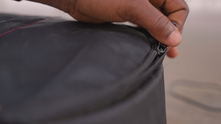 black fingers adjusting broken zipper on bag meticulous repair attempt indoors slow careful motion textured black nylon red seam tiny slider focus on fingers technique soft light patient mood