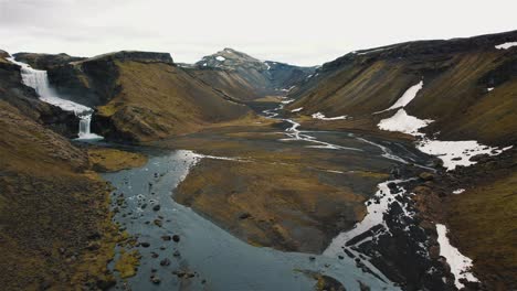 vuelo de drones que se eleva sobre un valle en islandia con un río y una cascada en 4k