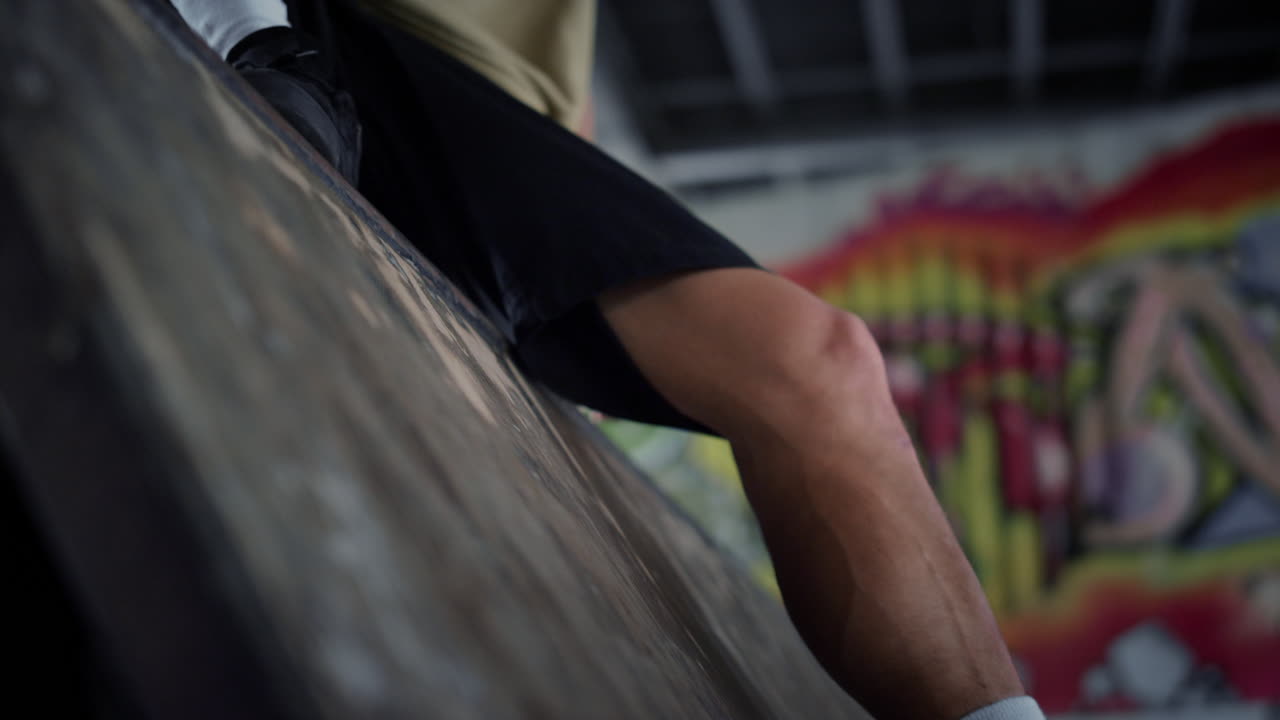 Unknown man having break after riding on skate board at skatepark with graffiti.