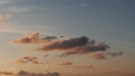 silhouette of airplane against colorful sunset fluffy clouds, wide shot panning left to right