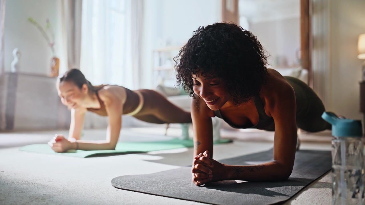 Diverse women doing plank exercise together home. Core fitness workout indoors.