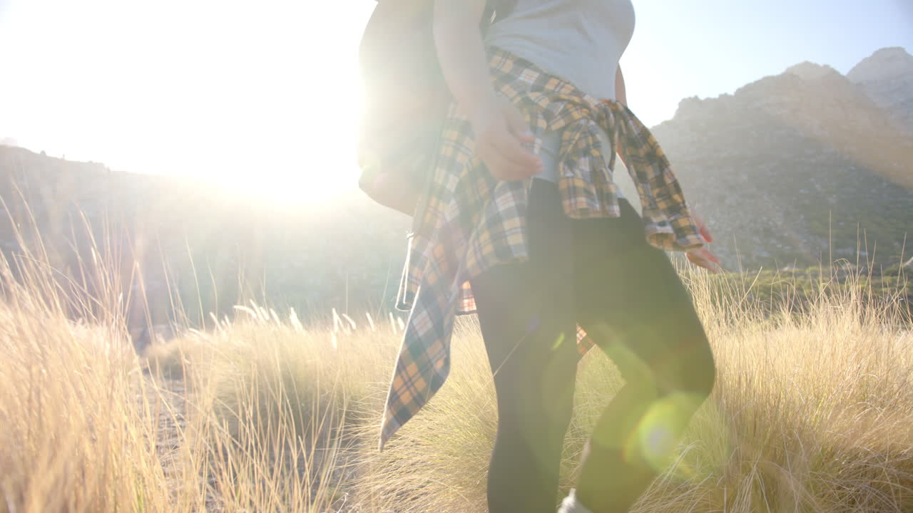 Hiking in mountains, woman with backpack walking through tall grass at sunrise