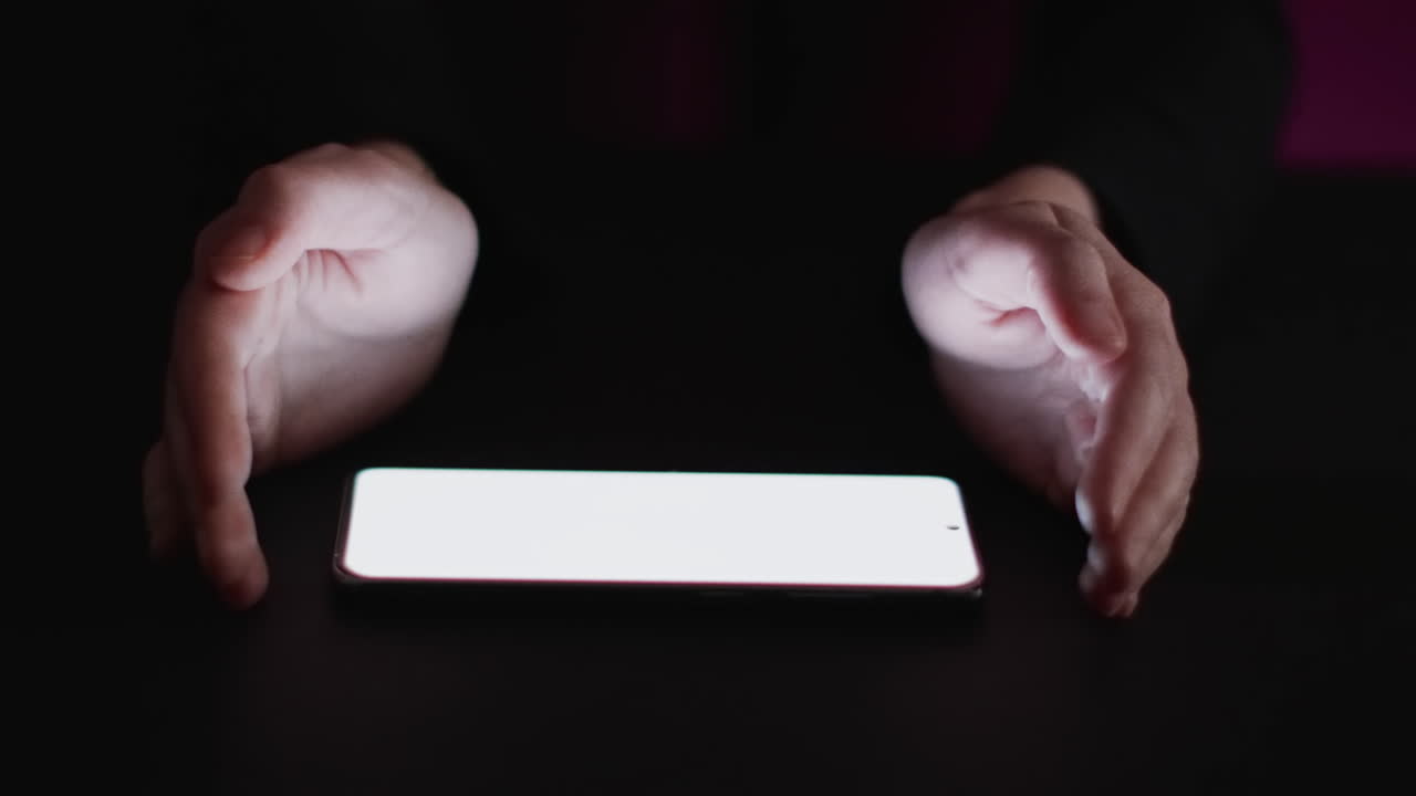 검은 바탕에 빈 화면을 가진 백인 남자의 손과 스마트 폰의 비디오
