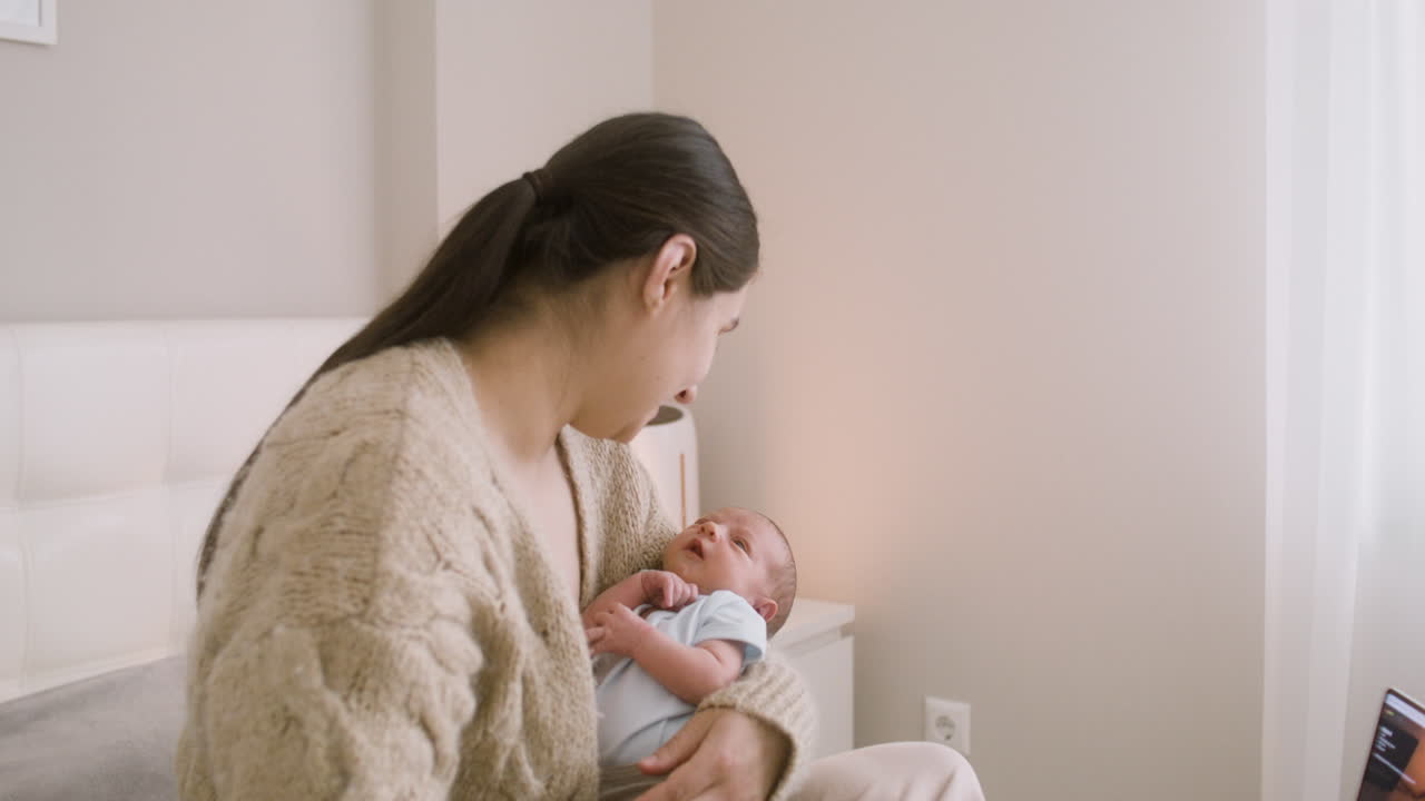 그녀의 아기를 안고 그와 이야기하는 침대에 앉아 갈색 머리 여자