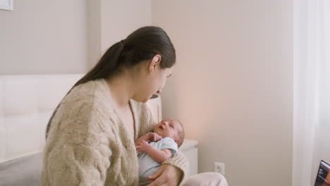 brunette woman sitting on the bed holding her baby and talking to him