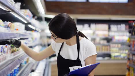 asian girl worker in and apron with a badge checks the goods on the shelves. re-inventory of goods, checking the expiration date