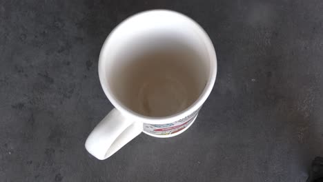 persona vertiendo agua caliente en una taza blanca