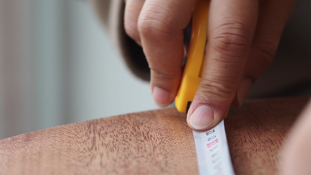 Hands Measuring a Wooden Surface with a Yellow Tape Measure