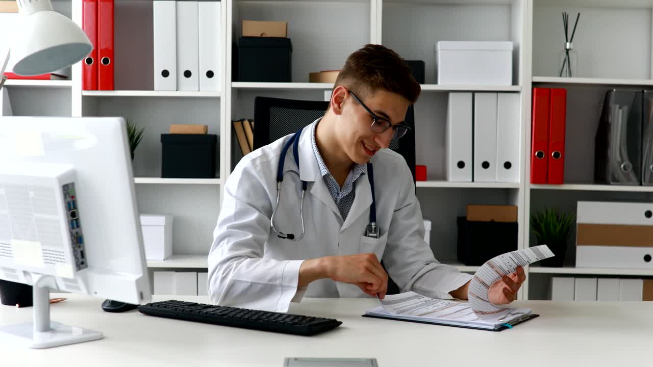 Giovane medico che esamina documenti e sorride alla fotocamera.