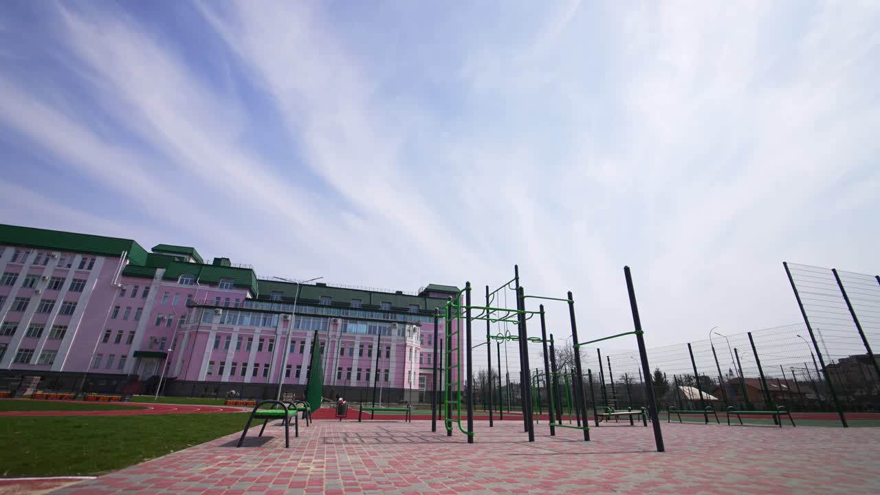 Huge pink building with sports ground in front of it. Sports horizontal bars and red running track for sport activities. Low angle view.