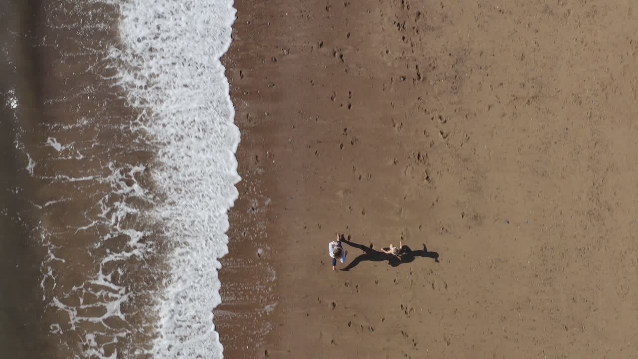 Ripresa con drone di una famiglia in vacanza che corre lungo la spiaggia vicino alle onde che si infrangono