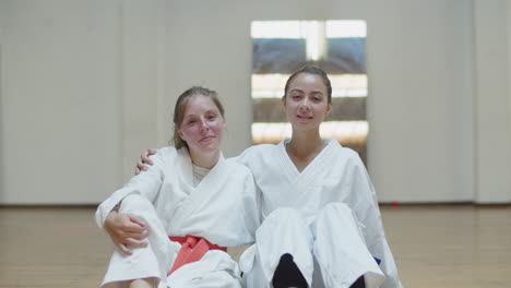 front view of happy girls in kimonos hugging and sitting in gym