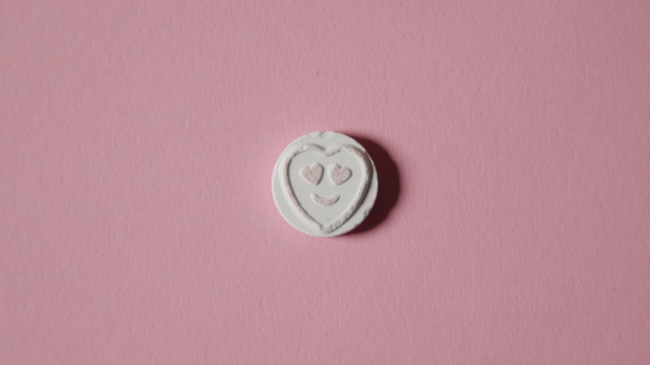 분홍색 배경에 사랑 이모지가 있는 하트 사탕을 손에 들고