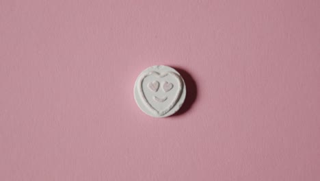 mano recogiendo dulces de corazón con amor emoji sobre fondo rosa