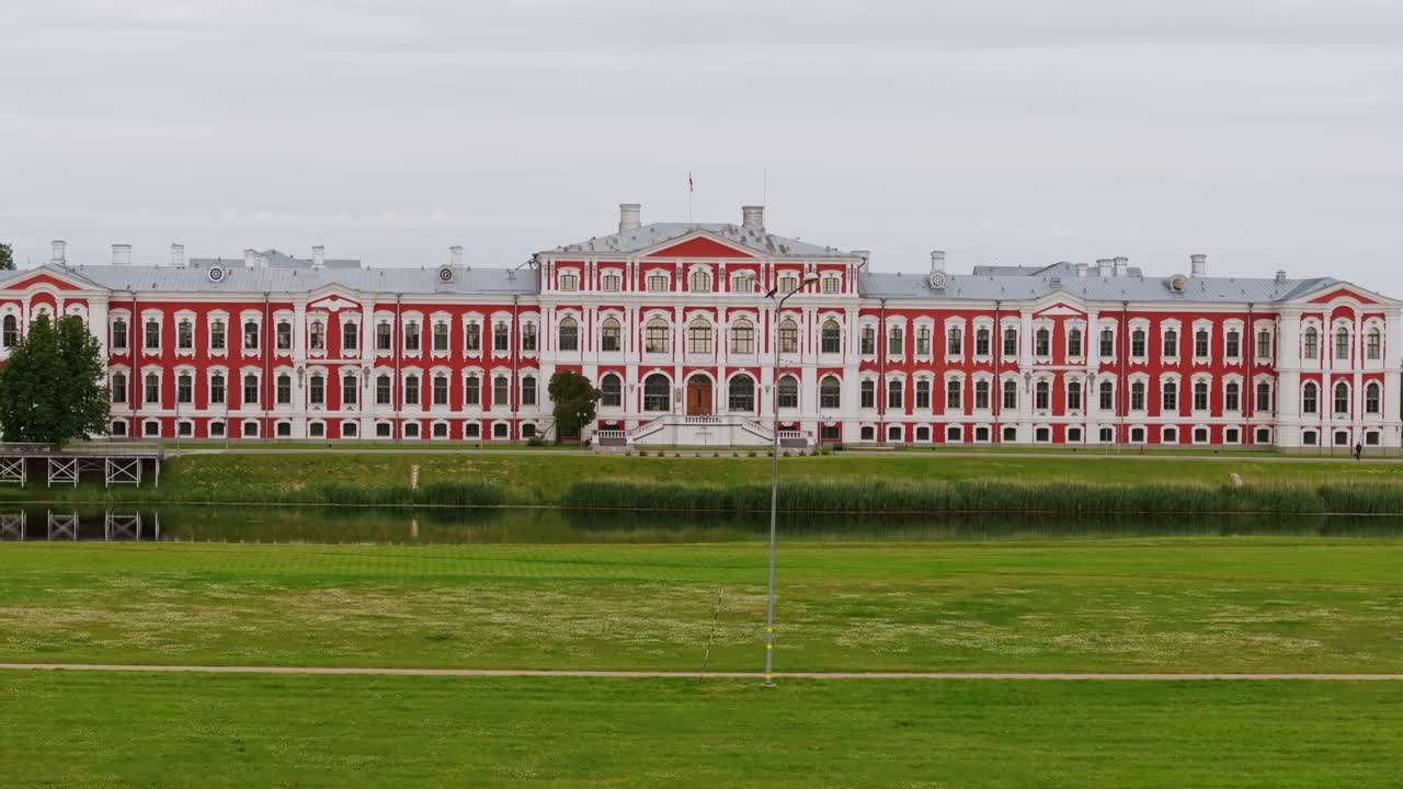 Drone glides left past red-white baroque palace during quiet summer sunrise