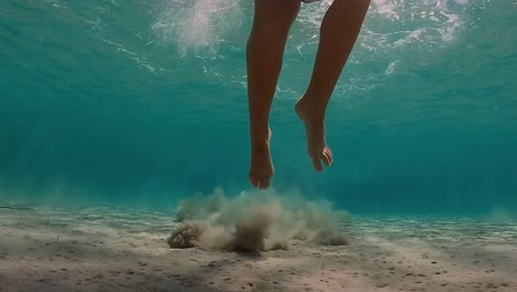 underwater scene of little girl jumps on seabed raising clouds of sand in transparent water