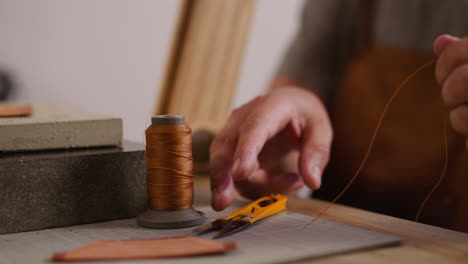 Tailor-cuts-waxed-thread-with-scissors-for-leather-in-shop