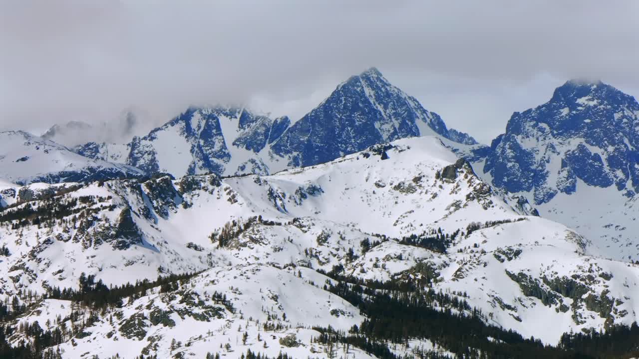 Pemandangan panorama pegunungan Minarets dengan puncak-puncak bergerigi yang menjulang tinggi dari titik pandang resor ski Mammoth Mountain, diambil dengan drone udara di California saat musim dingin dan semi, pagi hari cerah dengan langit biru di Hutan Nasional Inyo, geser ke kiri.