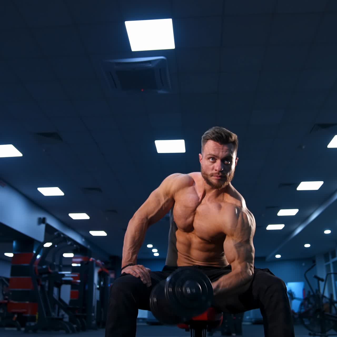 Bodybuilder atletico e potente che fa esercizi con i manubri. Corpo muscoloso da fitness su sfondo scuro di palestra. Rallentatore