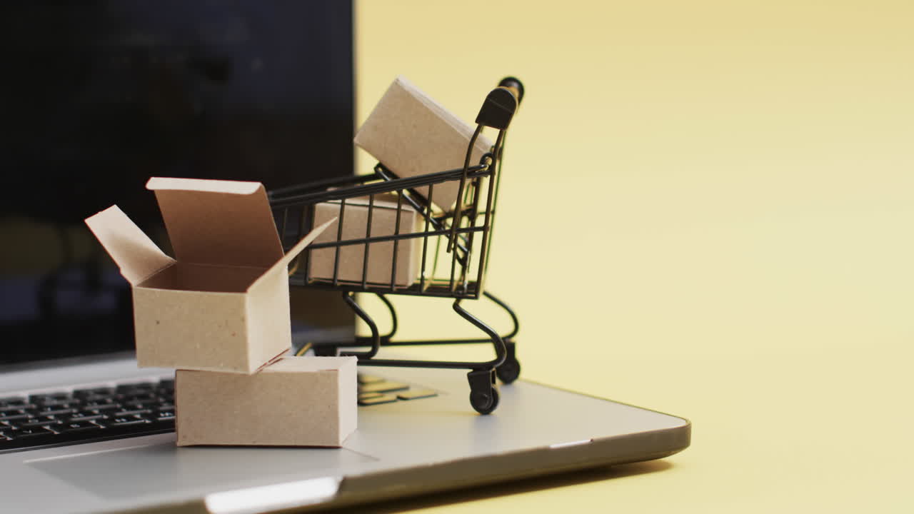 video de portátil con pantalla en blanco, carrito de compras y cajas con espacio de copia sobre fondo amarillo