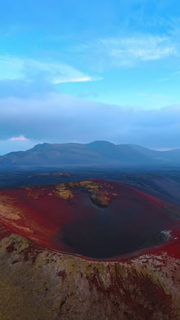 Distancing from the huge red volcano crater. Hazy barren landscape of Iceland with mountain range at backdrop. Vertical video.