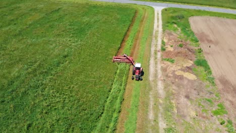 circling drone shot of red tractor in farm field harvesting hay