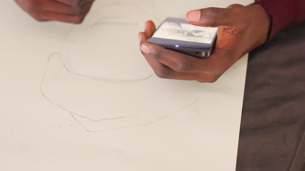 Black hand holds phone over paper, darkskinned hands alternate between thumb scrolling reference and pencil marking outline on white sheet, closeup of grip and screen glow, intimate creative moment