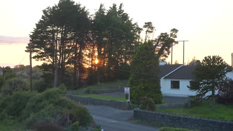 Fiery-orange-sunset-behind-trees-with-a-white-property-to-the-right-in-Clarinbridge,-Ireland