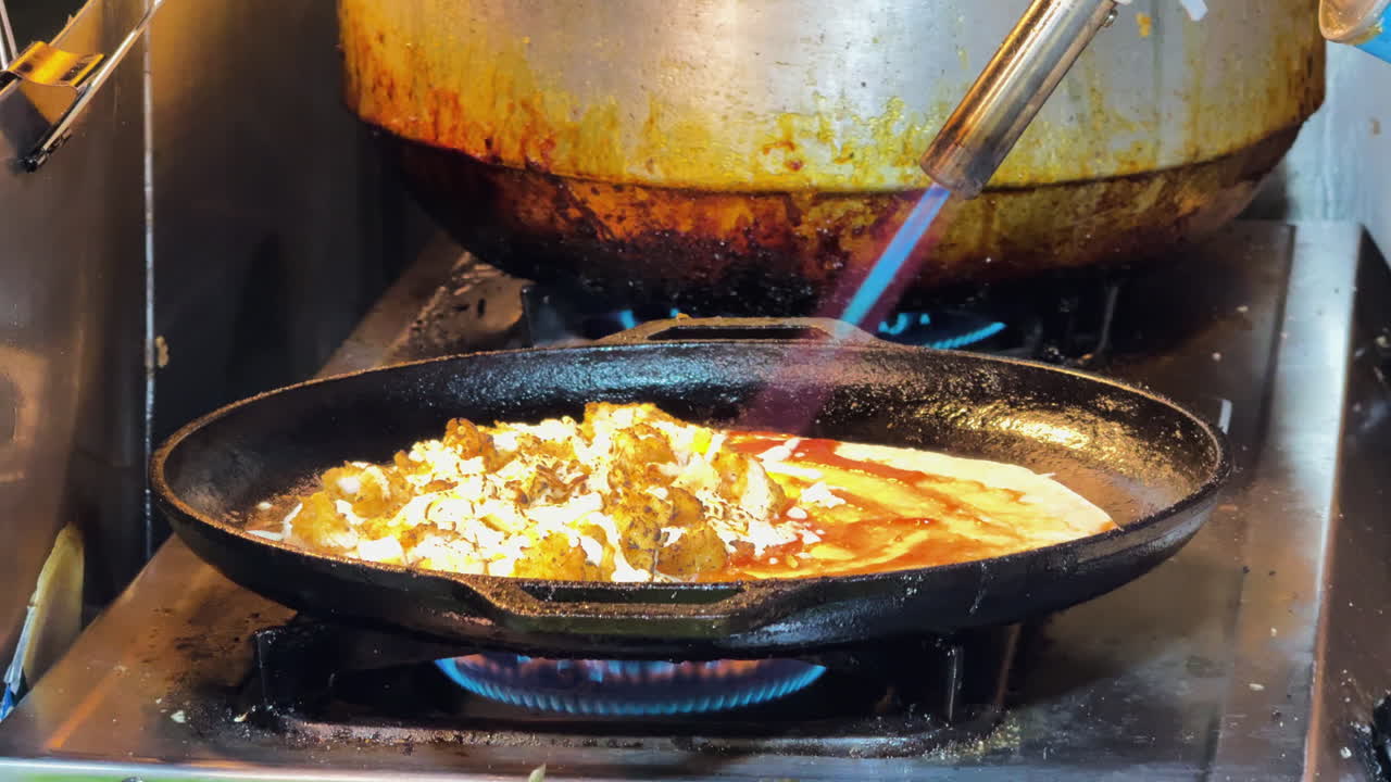 Close-up of food being browned with a blowtorch, stainless steel pot and kitchen tools in Watchediluang temple kitchen- Thailand