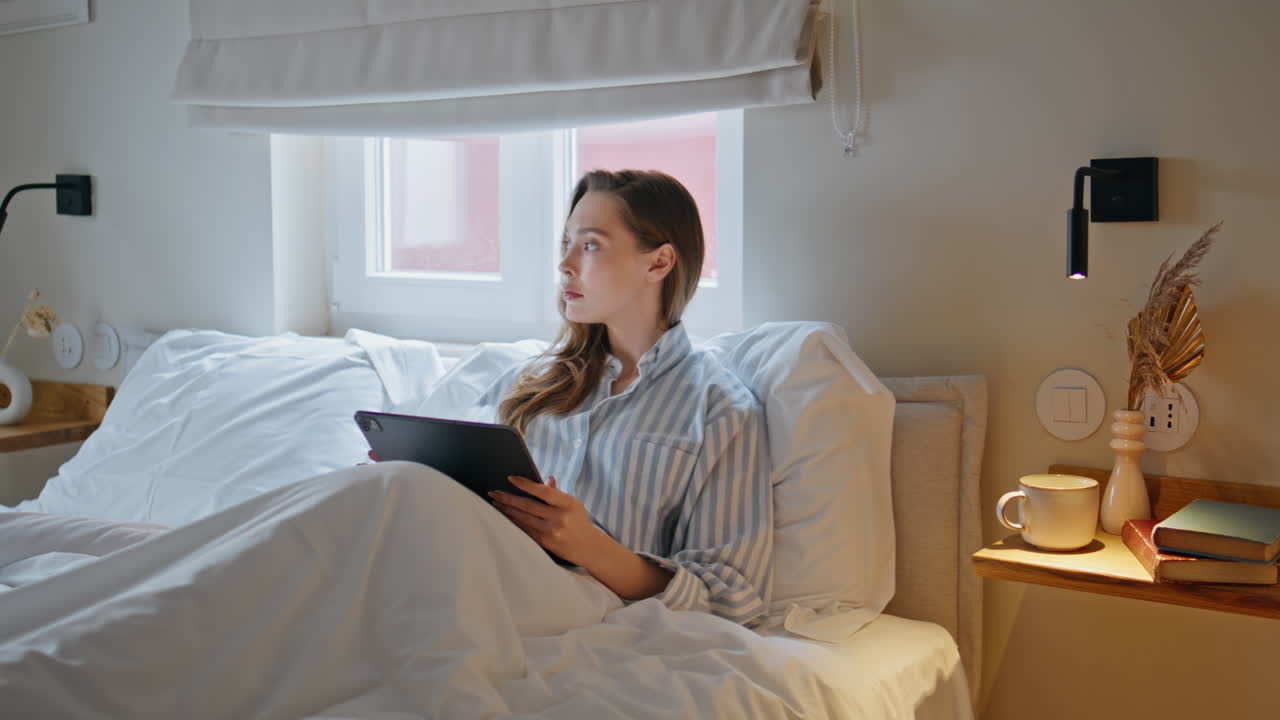Morning girl looking tablet relaxing in bedroom. Focused lady watching computer
