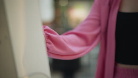 lady's hand in pink dress and black crop top seen operating something in front of her, with a blurred background well lights, slight blur view of people are walking in the background