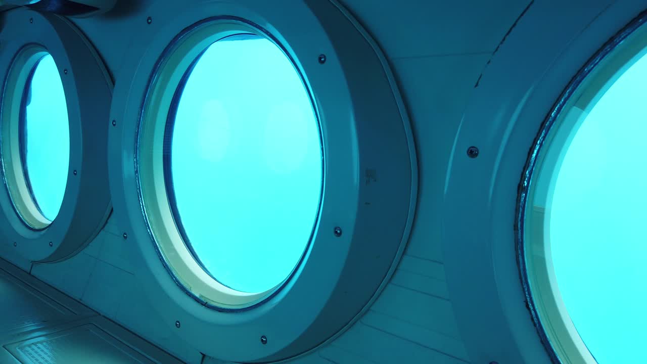 Gimbal panning shot across rows of portholes in a submarine at the bottom of the ocean off the coast of Kailua-Kona, Hawai'i