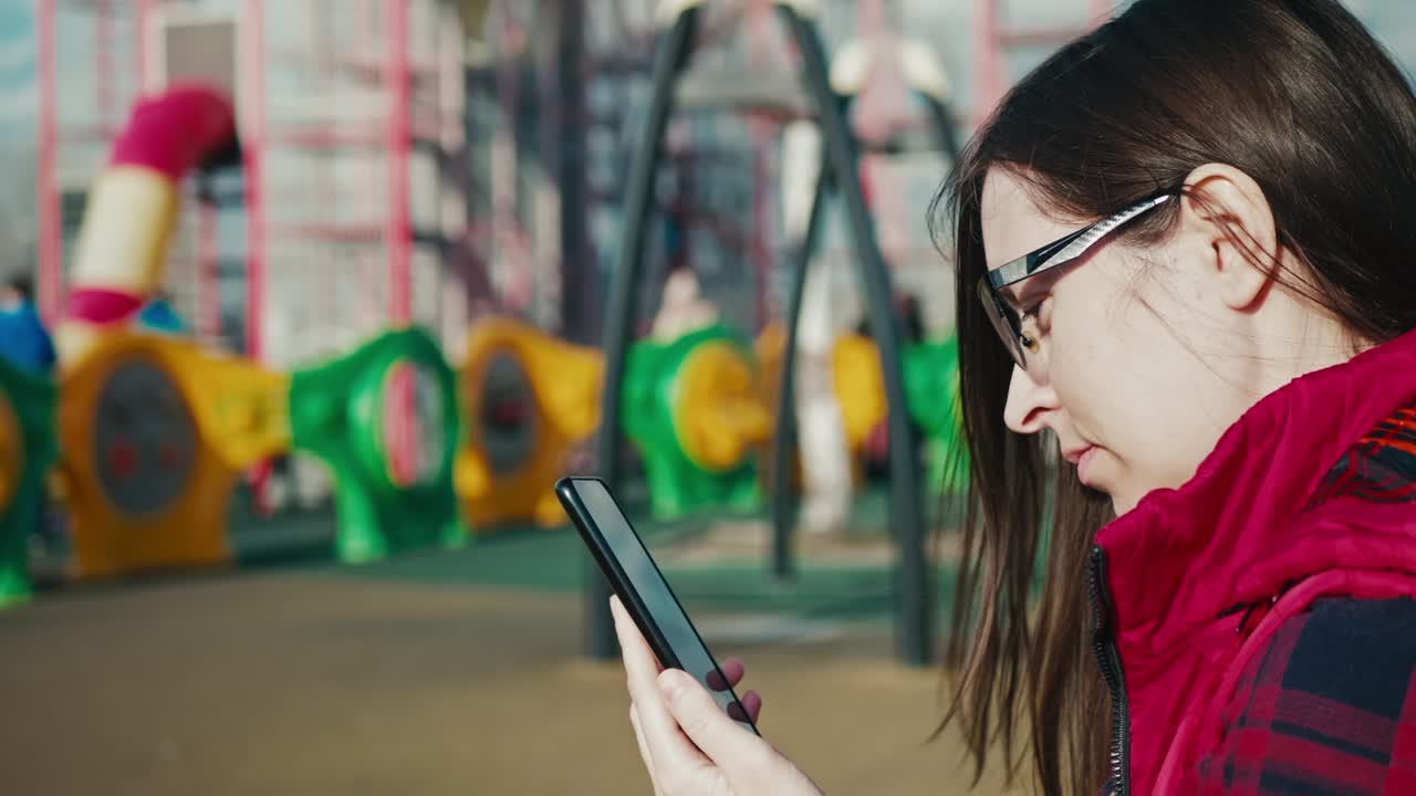 brunette mother uses smartphone at the playground