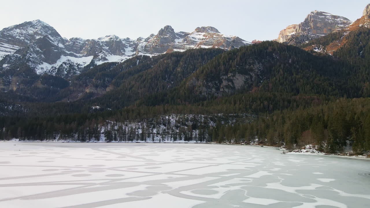 Ledové jezero s hustými lesními stromy a zasněženým pohořím Dolomitů v Trentinu v Itálii.