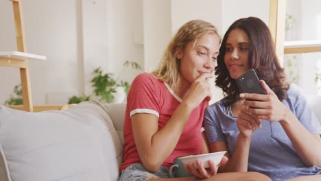 Two-young-woman-friends-talking-to-each-other-while-looking-in-a-smart-phone