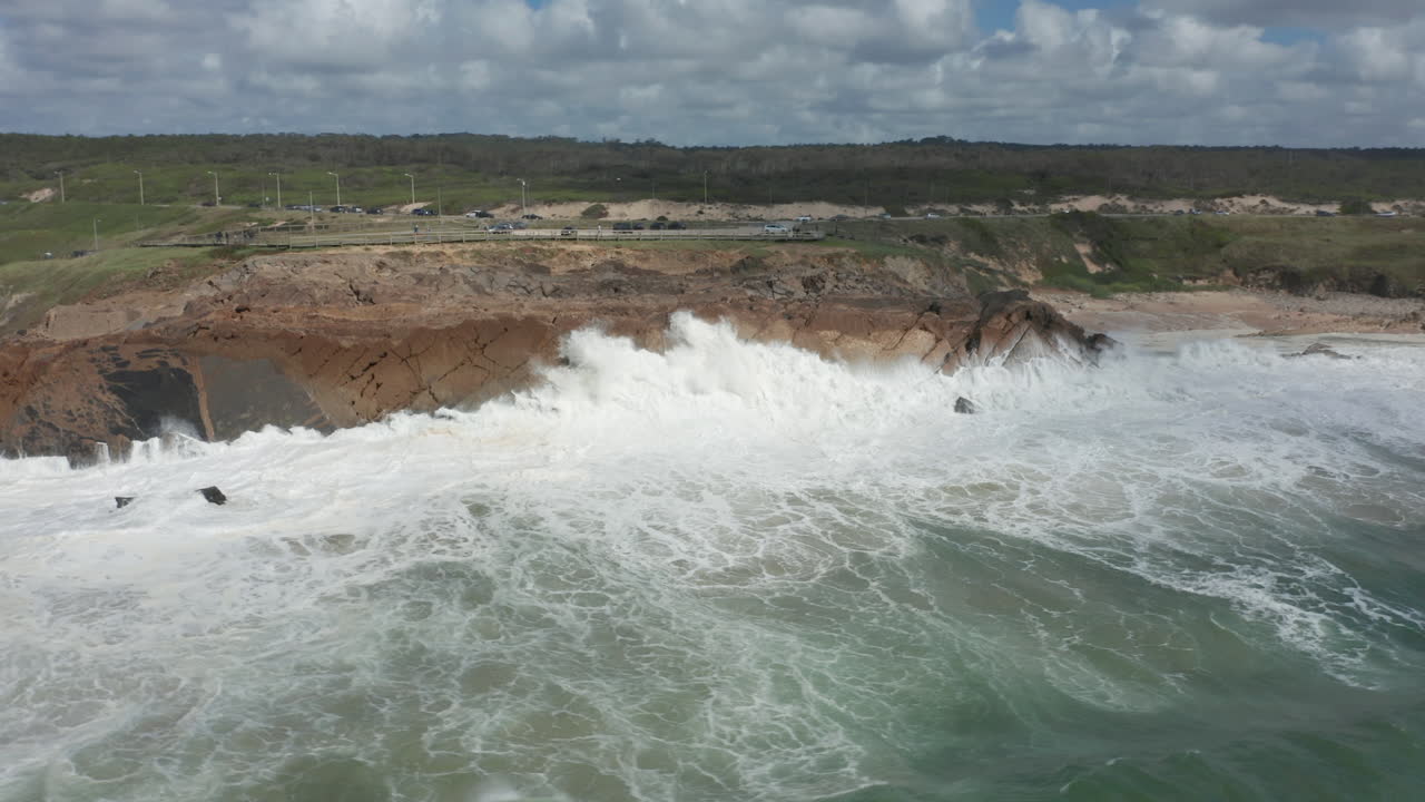 Aerial of rocky cliff with wild waves slamming into them. Drone turning and revealing long coastline