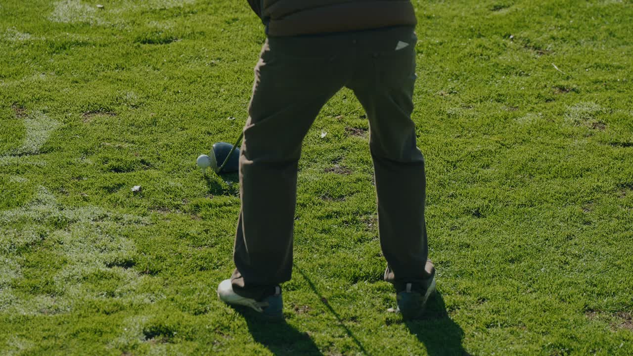 Parte inferiore del corpo di un golfista che si prepara a colpire la palla su un tee di legno usando un driver prima dello swing