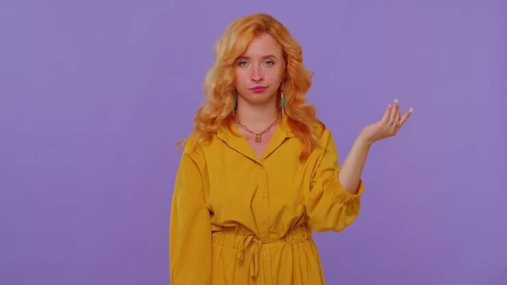 Ragazza dai capelli rossi in vestito che punta il dito verso la fotocamera, mostrando un gesto sciocco e incolpando qualche idiota per un piano folle.