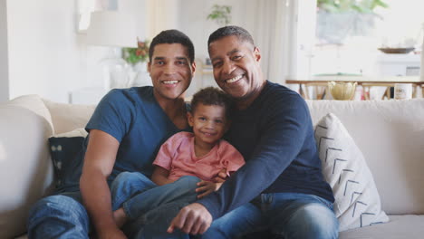 Three-generation-male-family-group-sitting-on-a-sofa-together-smiling-to-camera