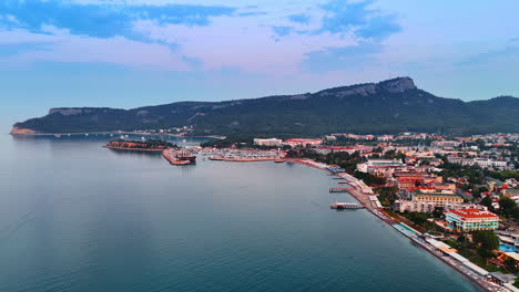 resort town with hotels, beach line and berths. wooded green mountain range at backdrop. sunset in the mediterranean coast of turkey. aerial view