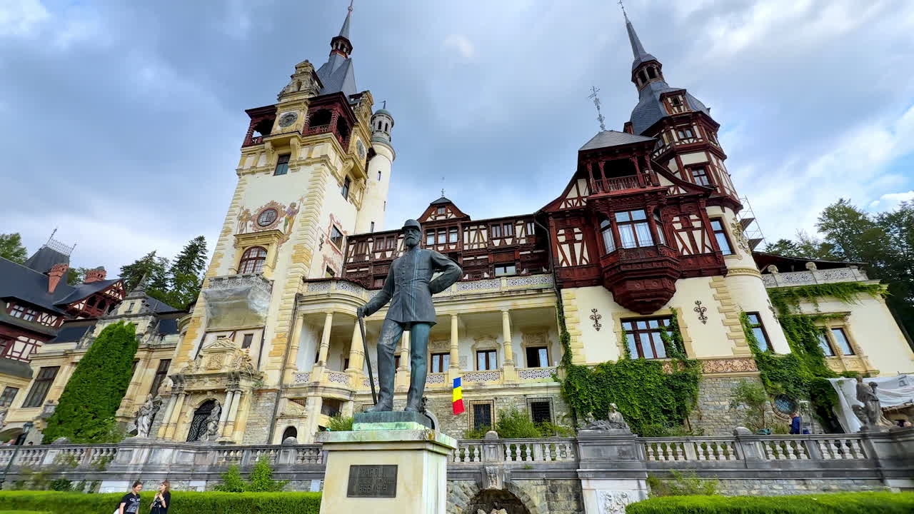 Statue of Carol I outside the beautiful palace. Pele? Castle in the Carpathian Mountains, Romania at backdrop. Low angle view at the background of the overcast sky