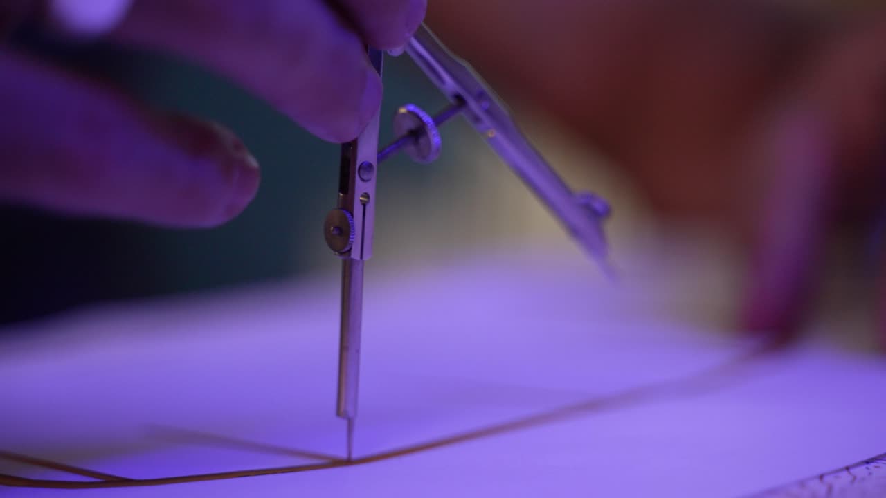 Close up of a man adjusting a compass and measuring points on a technical drawing with the compass while making marks on the drawing with a pencil at the allocated points that the compass has measured