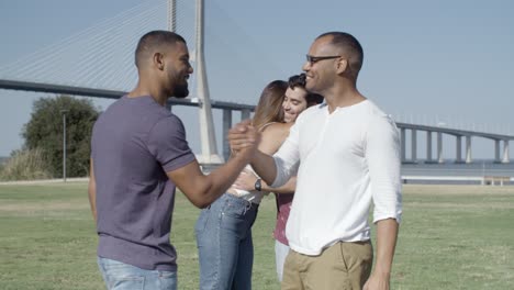 amigos sorridentes a encontrarem-se no prado verde durante um dia ensolarado.