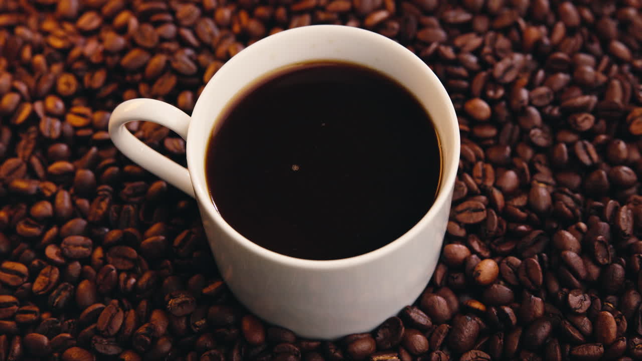 Taza de café blanca con café solo caliente sobre granos tostados