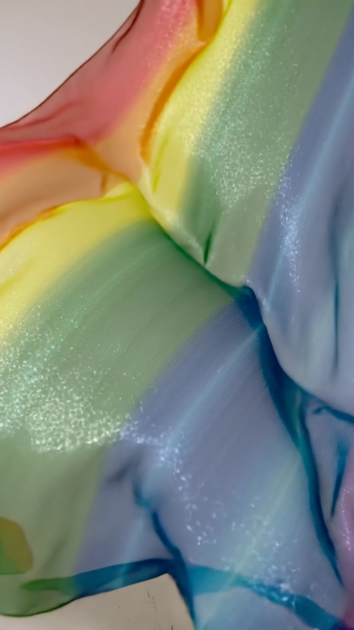 Vertical video: Off-screen pull moving rainbow scarf across white wall, showing shimmer for fashion