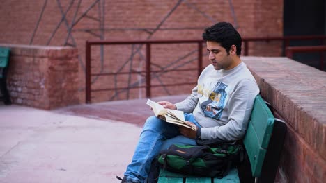 Male-Bookworm-Enjoying-Nature-While-Reading,-Young-South-Asian-Man-Engrossed-in-Reading-Outdoors