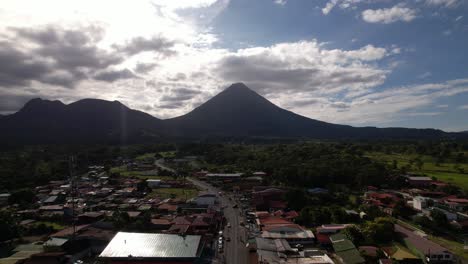 drone flying backwards revealing rural local village and huge volcano