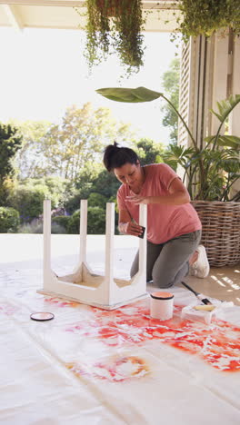 vertical video: painting wooden stool, woman kneeling on floor with paint supplies