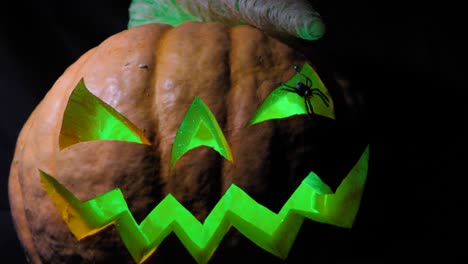 halloween pumpkin with a scary face and a spider on the eye, illuminated from the inside multicolored lights, a very scary pumpkin for halloween